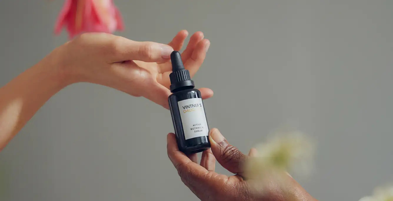 Two hands hold a bottle of Vintner’s Daughter Active Botanical Serum with a pipette.