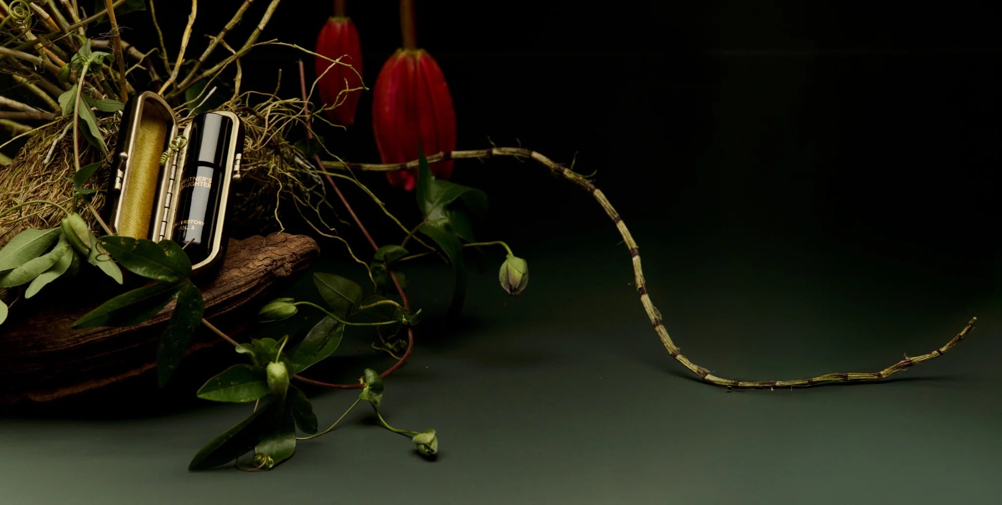 Alt: Vintner’s Daughter Active Botanical Serum in a luxury travel case, surrounded by botanical elements and exotic flowers on a dark green background.